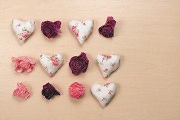 Hearts and wilted roses on pastel wooden background.