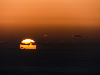 Fototapeta na wymiar Glowing sun ball sinking in the ocean in striking orange colours.