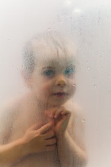 Baby in the shower behind glass with drops