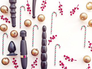 Sex toys, golden christmas balls, candies and branches with red berries are on a white background