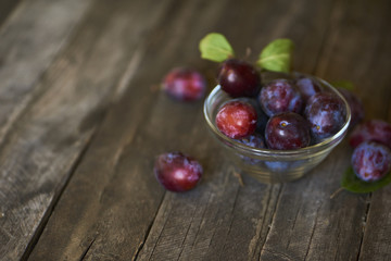 Fresh plums in plate on wooden background