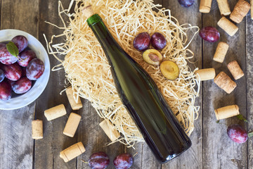 Fototapeta na wymiar Bottle of wine with fresh plums in plate and corks on wooden background