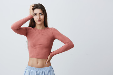 Obraz premium Young beautiful dark-haired caucasian girl with long hair in fashionable outfit with opened belly holding hand on forehead, looking aside with foxy expression, thinking about cheating on exams.