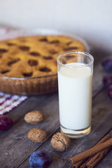 Glass of milk with homemade plum pie on rustic background