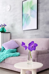 Lilac accent in modern interior. Table with flowers and comfortable couch in living room