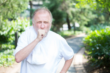 Closeup portrait, senior guy holding towel, very tired, exhausted from over exertion, coughing catching breath, isolated outdoors outside green trees background