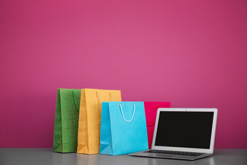 Laptop and shopping bags on table against pink background