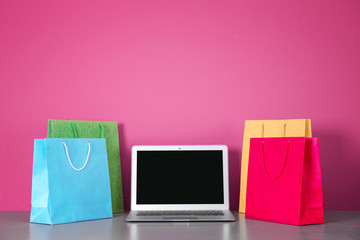 Laptop and shopping bags on table against pink background