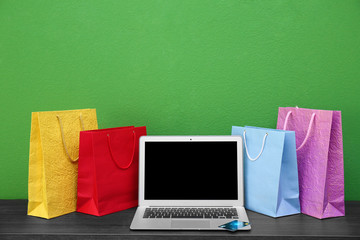 Laptop and shopping bags on table against green background