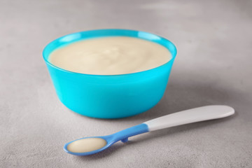 Spoon and bowl with baby porridge on table