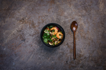 Spicy Thai soup Tom Yam with seafood in a black bowl on a vintage colored background with a wooden spoon. Top view