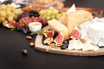 different kinds of cheeses, honey, figs, nuts, grapes, and fruit on a table. Selective focus. Copy space.