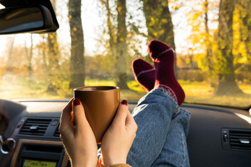 Autumn car trip. Woman feet in warm wool socks and cup of tea in the car