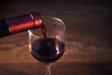 Pouring red wine into the glass against wooden background