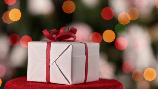 Christmas present spinning in front of blinking lights on xmas tree backround - closeup, camera slide