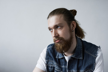 Fototapeta premium Studio shot of attractive fashionable European student with bushy beard and hair bun rolling eyes while feeling bored during dull tiresome lecture at college. Human facial expressions and emotions