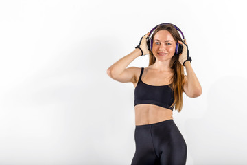 Dark hair girl, wearing a black top and leggins, is listening to music in headphones in the white isolated background