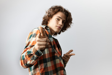 Half profile of handsome self confident guy dressed stylishly staring and pointing at camera, having mysterious cute smile while dancing indoors, posing at copy space studio wall for your content