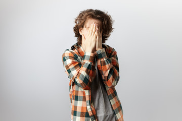 Unrecognizable young man dressed in trendy checkered shirt over grey t-shirt covering face with...