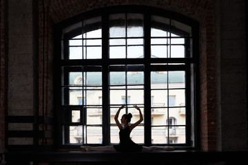 Silhouette of attractive slim flexible young European female ballet dancer girl wearing black tutu and pointe shoes raising her slender arms while stretching at large window, doing right split © Anatoliy Karlyuk