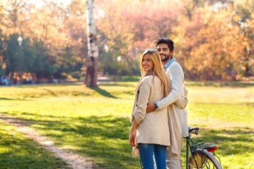 Young couple with bicycle walking in park on sunny autumn day.