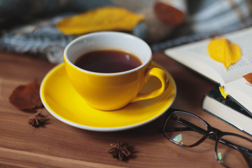 Autumn mood. Yellow cup with hot tea and book on the wooden surface.
