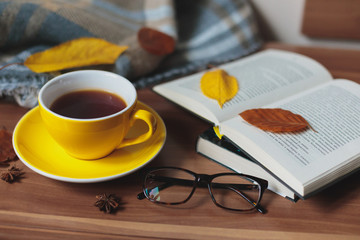 Autumn mood. Yellow cup with hot tea and book on the wooden surface.