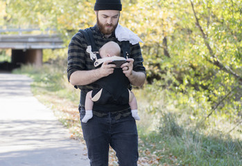 Millennial Dad with Baby in Carrier Outside Talking and Texting on a Beautiful Fall Day