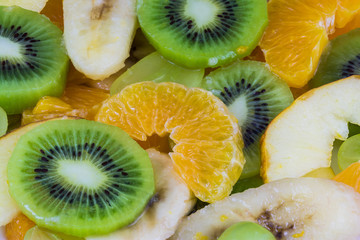 Close-up of sliced kiwis and oranges on a fruit salad background. Green and yellow texture from the juicy fruit blend full of vitamins.
