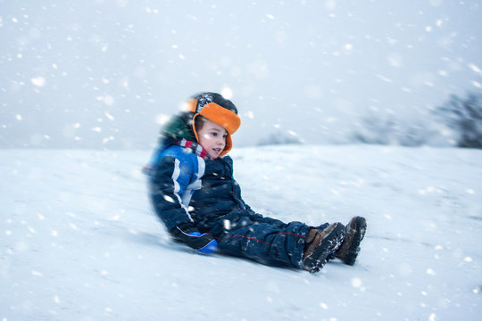Excited boy sledding downhill on a snowy day.