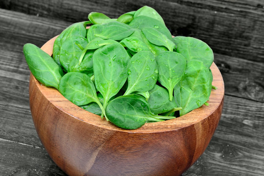 Fresh green baby spinach leaves in a bowl on wooden table