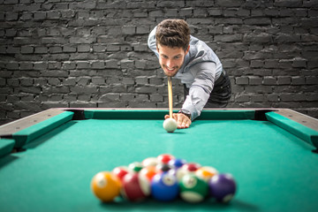 Happy business man playing a game of billiards and preparing to break pyramid of balls on the pool...