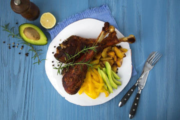 Baked turkey legs with potatoes, avocado and paprika on a blue wooden background