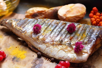 Grilled fish with cheese, honey, rowan, kalina, lemon slices, baked potatoes, pink flowers and spices on parchment paper