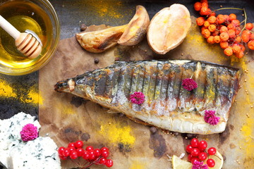 Grilled fish with cheese, honey, rowan, kalina, lemon slices, baked potatoes, pink flowers and spices on parchment paper