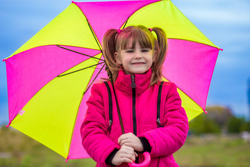 Funny cute girl with colorful umbrella playing in the garden by rainy autumn day