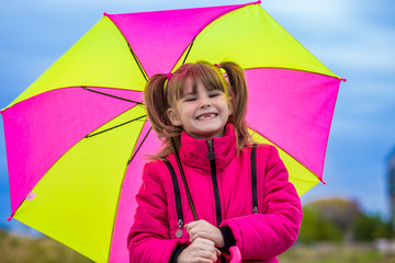 Funny cute girl with colorful umbrella playing in the garden by rainy autumn day
