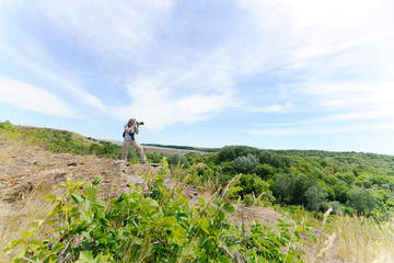 Obraz premium Photographer of wild nature young man in arafatke shoots on camera landscape against nature and rocks