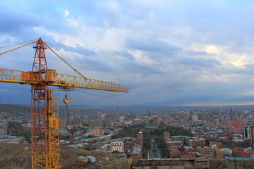 Fototapeta na wymiar orange high construction crane against the background cityscape, of the blue sky and clouds