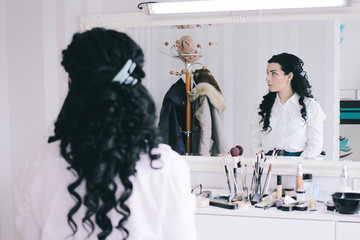 beauty salon, girl with long black hair sits at the mirror in the beauty studio, curly haired brunette expects a make-up artist in the hairdressing salon, looking away