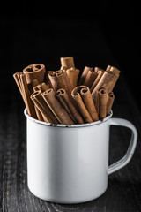 Taza de porcelana con palitos de canela en rama sobre fondo de madera negro