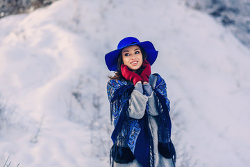 Fototapeta na wymiar Young beautiful stylish girl in blue hat and scarf on the background of snowy hill.