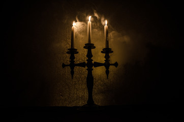 burning old candle vintage wooden candlestick. on dark toned foggy Background.