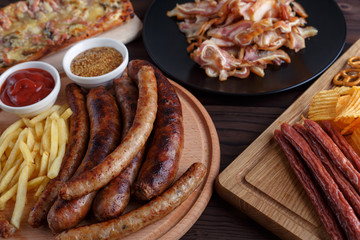 Appetizing beer snacks close up. Grilled sausages with french fries and sauces, salami, chips, pretzel crackers on wooden boards.Oktoberfest food, pub concept