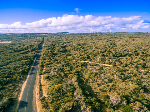 Aerial view of road in beautiful Australian countryside on bright summer day with wind farm in the distance © Greg Brave