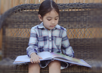 little girl reading book on bench at backyard , filtered tones