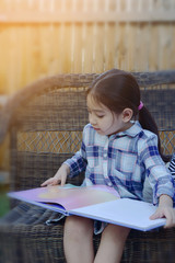 little girl reading book on bench at backyard , filtered tones