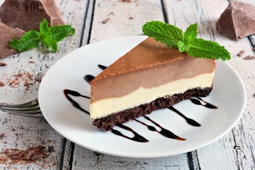 Slice of chocolate vanilla cheesecake on plate against a rustic white wood table