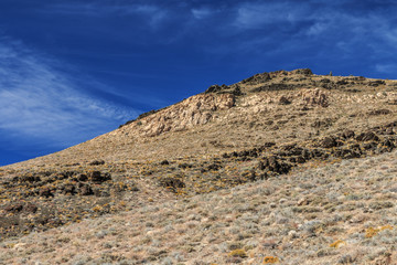 Fototapeta na wymiar A desert landscape with sage and rocky cliffs stand in front of a blue sky with wispy clouds