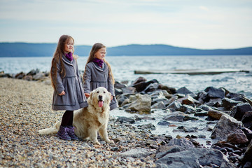 Two little twin sisters on a walk with dog on the beach.